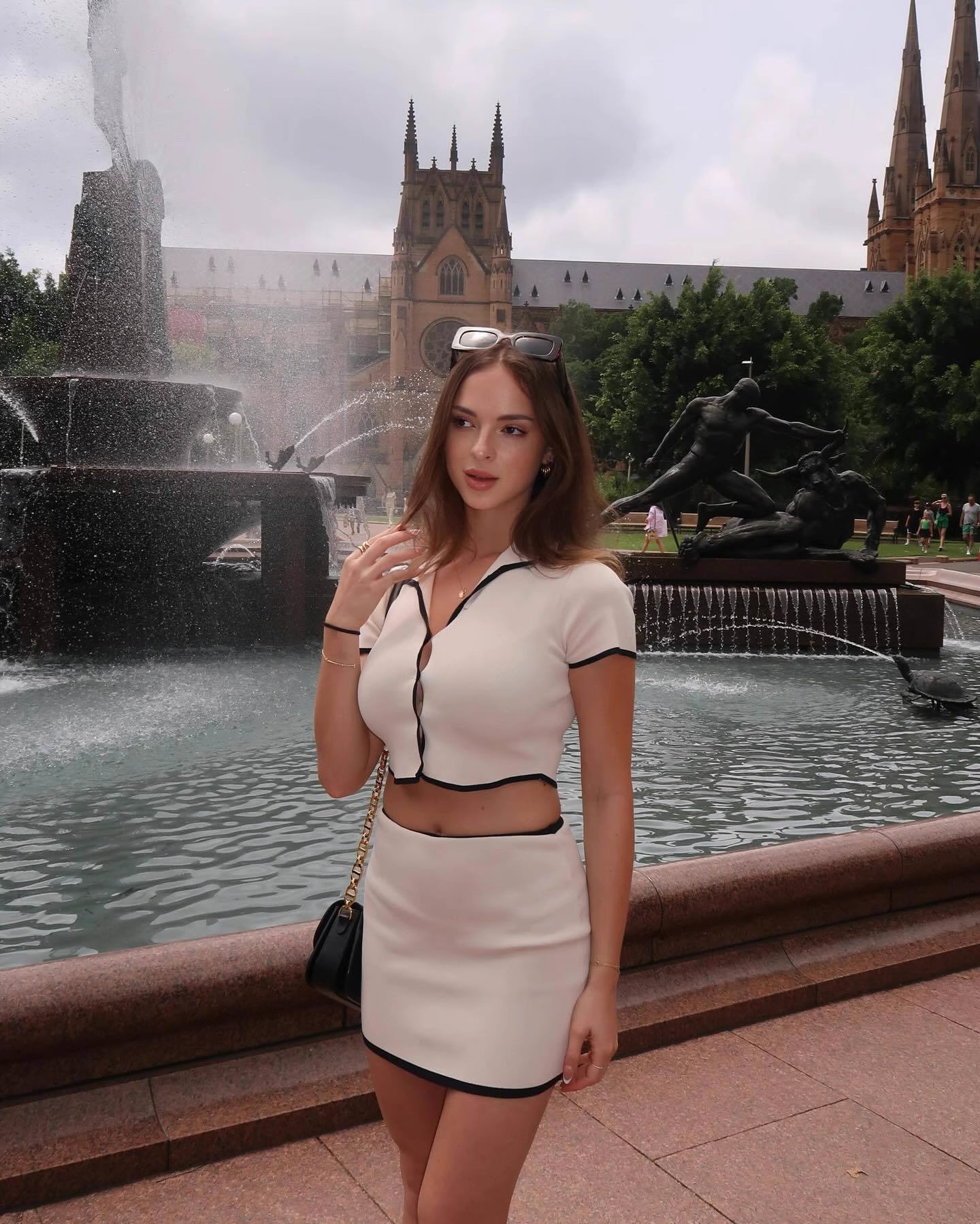 Woman wearing Orchid Moda beige desert co-ord set with black trim standing by a city fountain