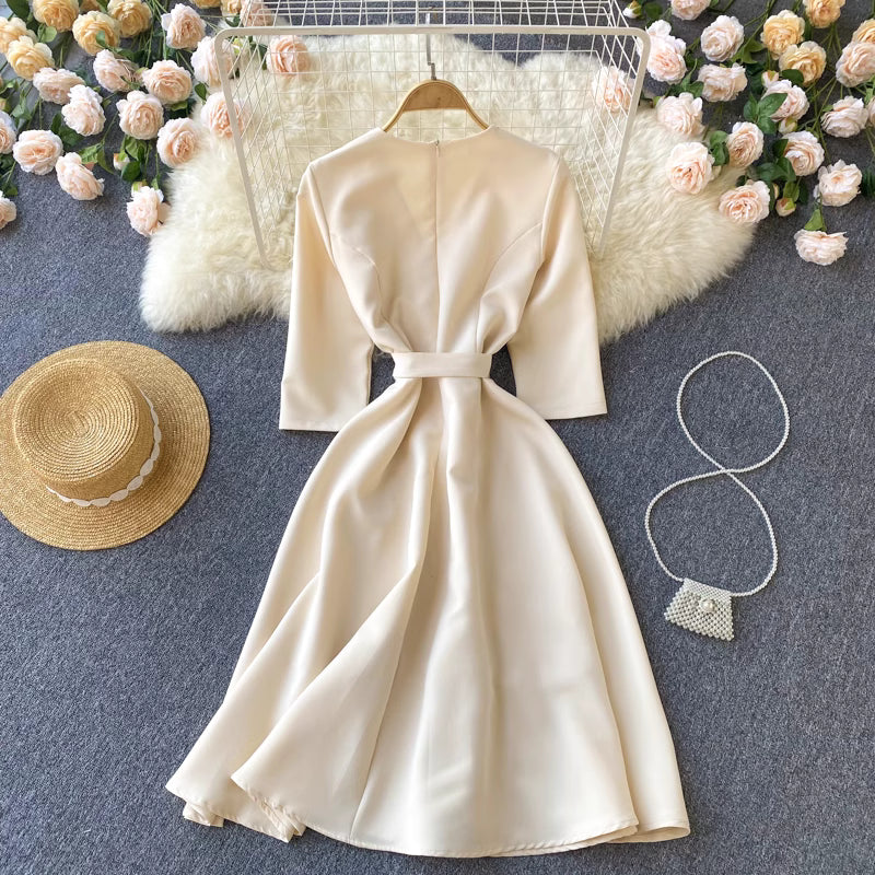 Orchid Moda almondine midi dress in beige with belt detail displayed with straw hat and pearl purse