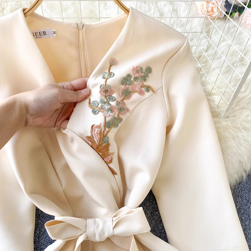 Close-up of Orchid Moda almondine midi dress in cream with floral embroidery and tied waist bow