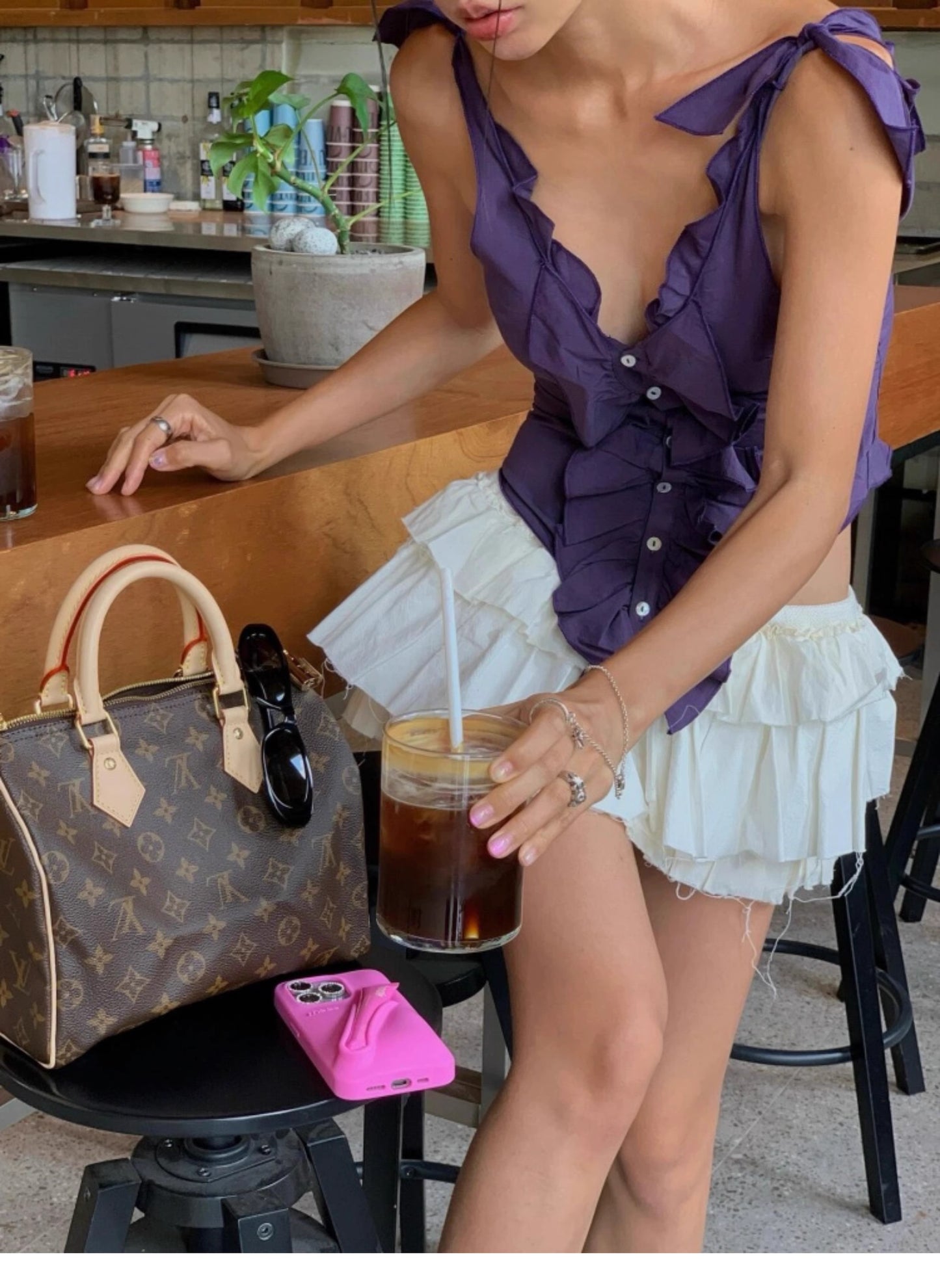 Woman wearing a purple ruffled cami top for women with tied shoulder straps and white layered skirt holding iced coffee