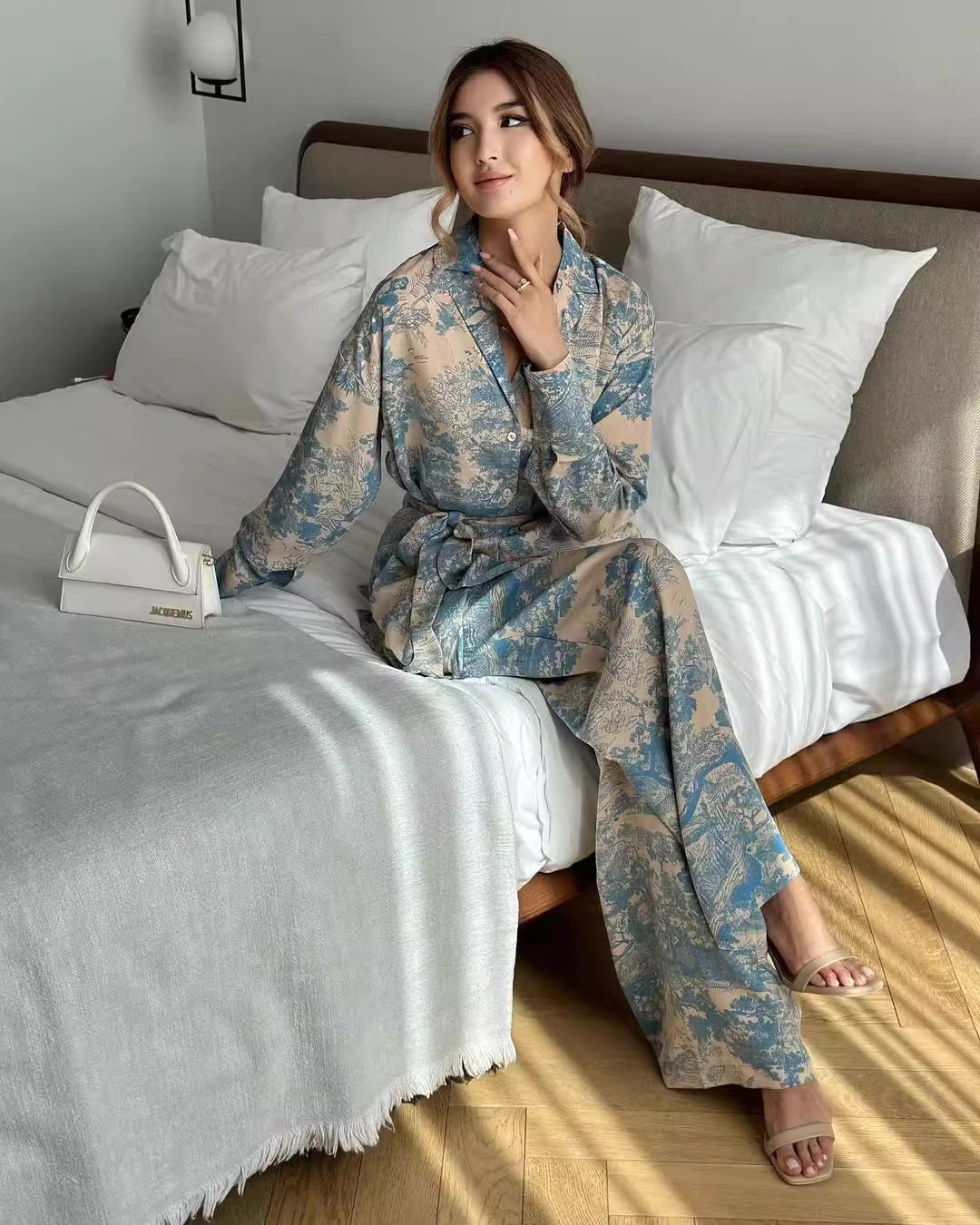 Orchid Moda women's co ord set with floral print worn by model sitting on bed with white handbag
