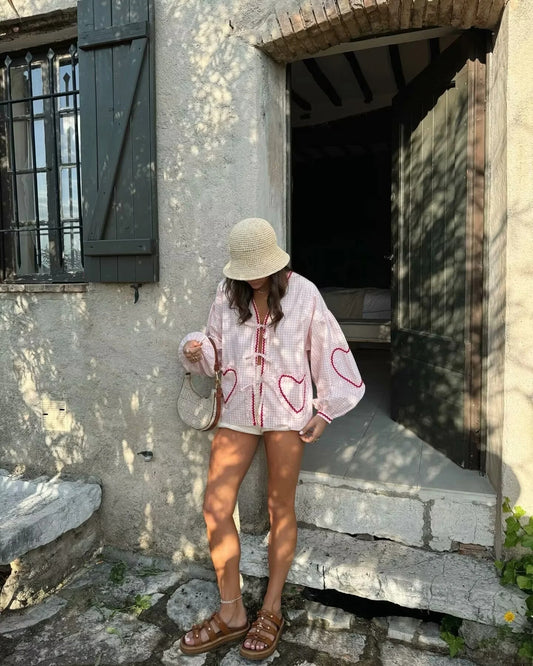 Woman wearing Orchid Moda gingham heart print top with red hearts, paired with a beige hat and brown sandals