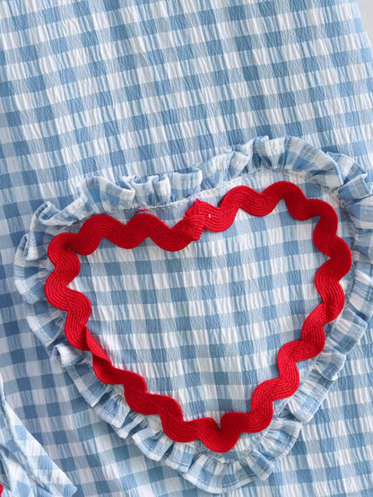 Close-up of blue and white gingham fabric with ruffled trim and red rickrack heart detail on gingham heart print top