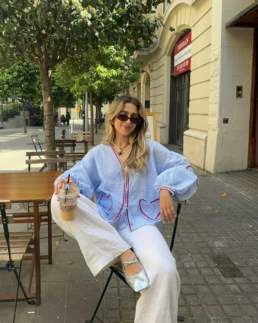 Woman wearing a gingham heart print top with blue and white check pattern sitting outdoors holding iced coffee