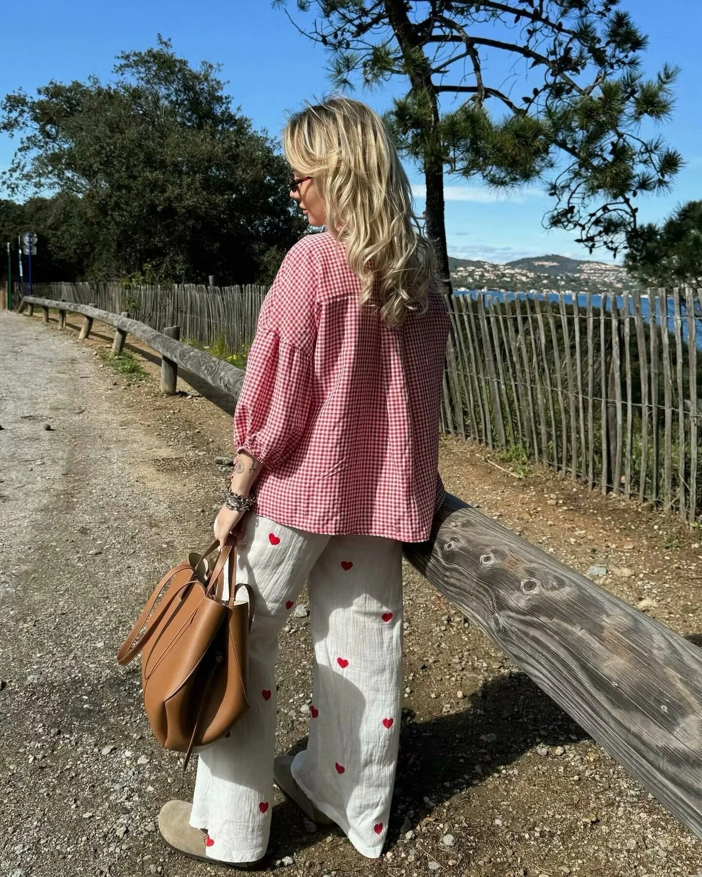 Woman wearing Orchid Moda gingham heart print top in red and white outdoors by wooden fence