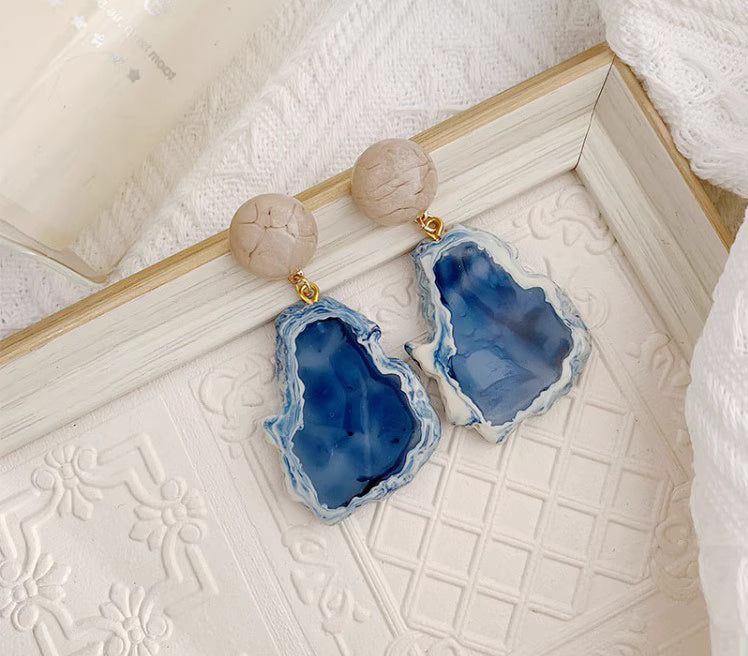 Orchid Moda blue statement earrings with natural stone design and gold accents on white textured background