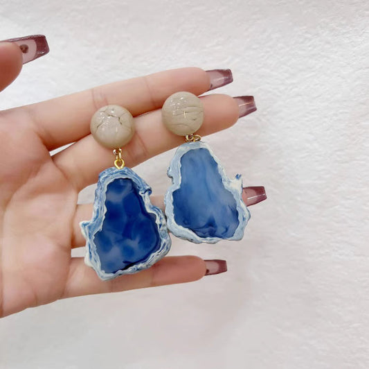 Orchid Moda blue statement earrings with natural stone design in hand against white background