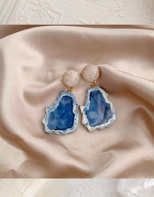 Orchid Moda blue statement earrings with marble-like studs and irregular blue resin drops on satin fabric