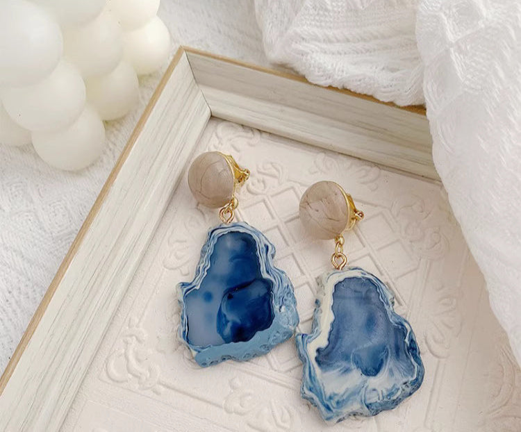 Orchid Moda blue statement earrings with irregular stone shapes and gold accents on white textured background