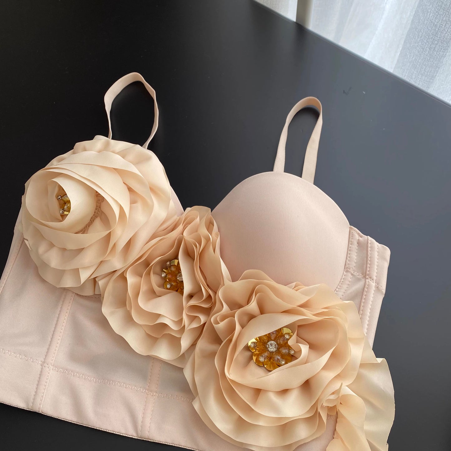 Orchid Moda blush corset top with large 3D flower embellishments and gemstone details on black surface