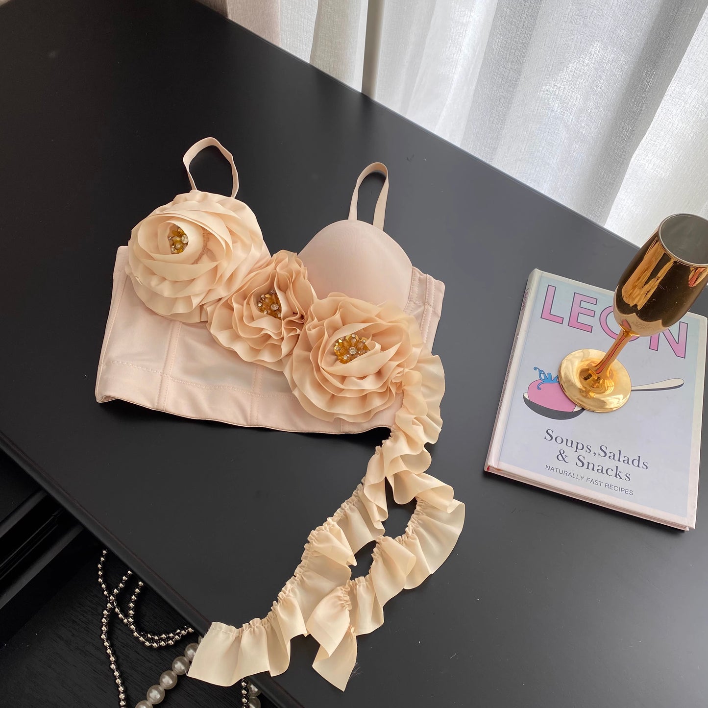Orchid Moda blush corset top with floral appliques and ruffled detail on black table next to book and gold glass