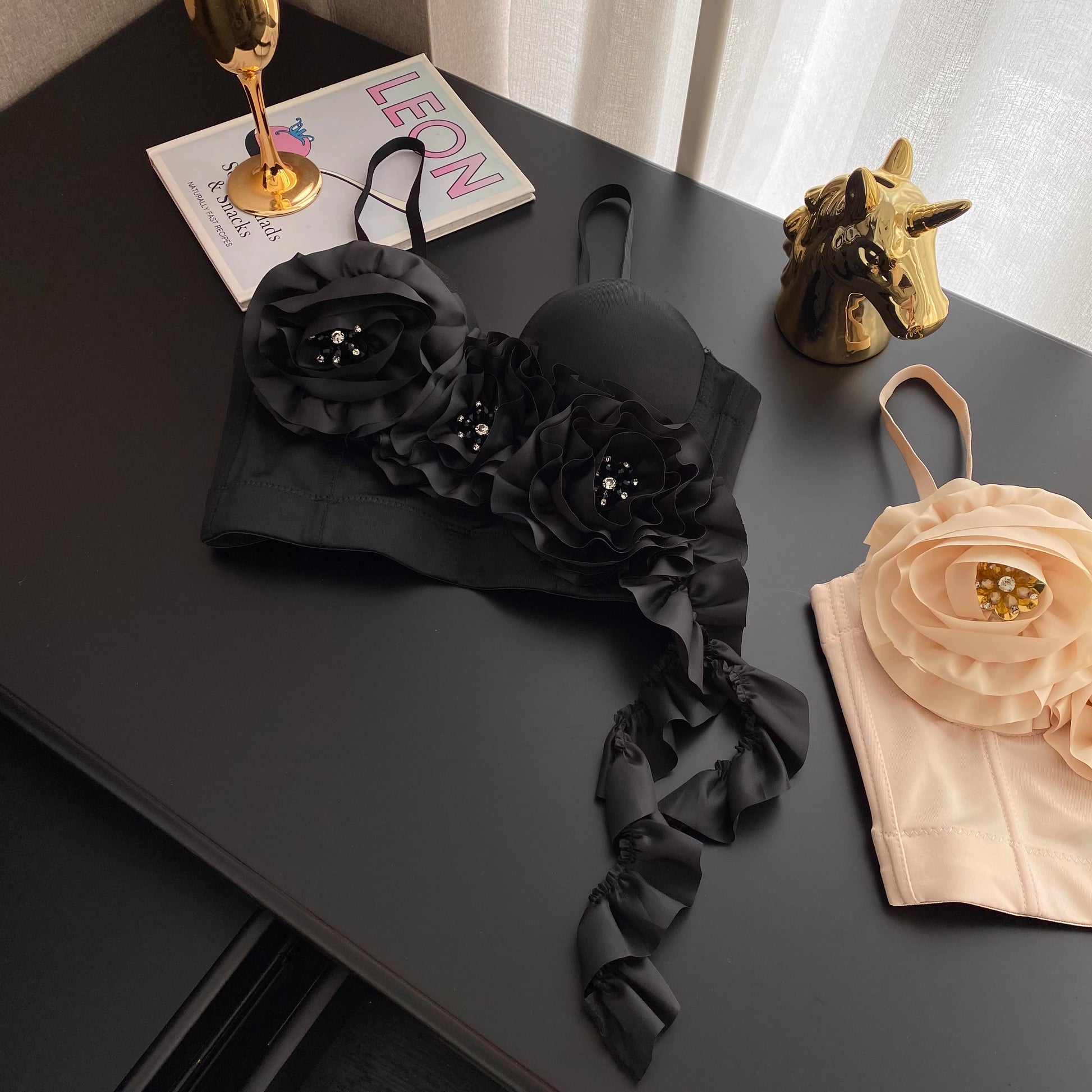 Black blush corset top with large floral embellishments and decorative beads on a black surface