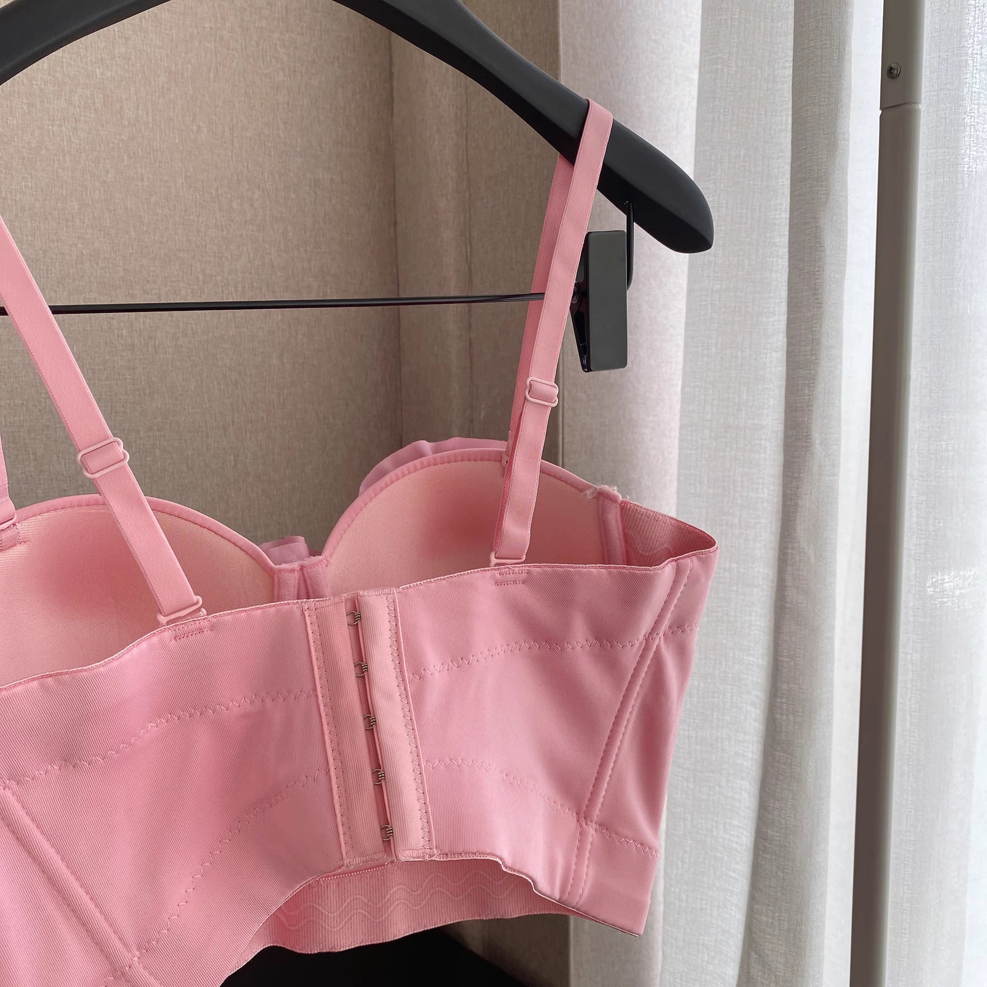 Orchid Moda blush corset top with adjustable straps hanging on black hanger indoors