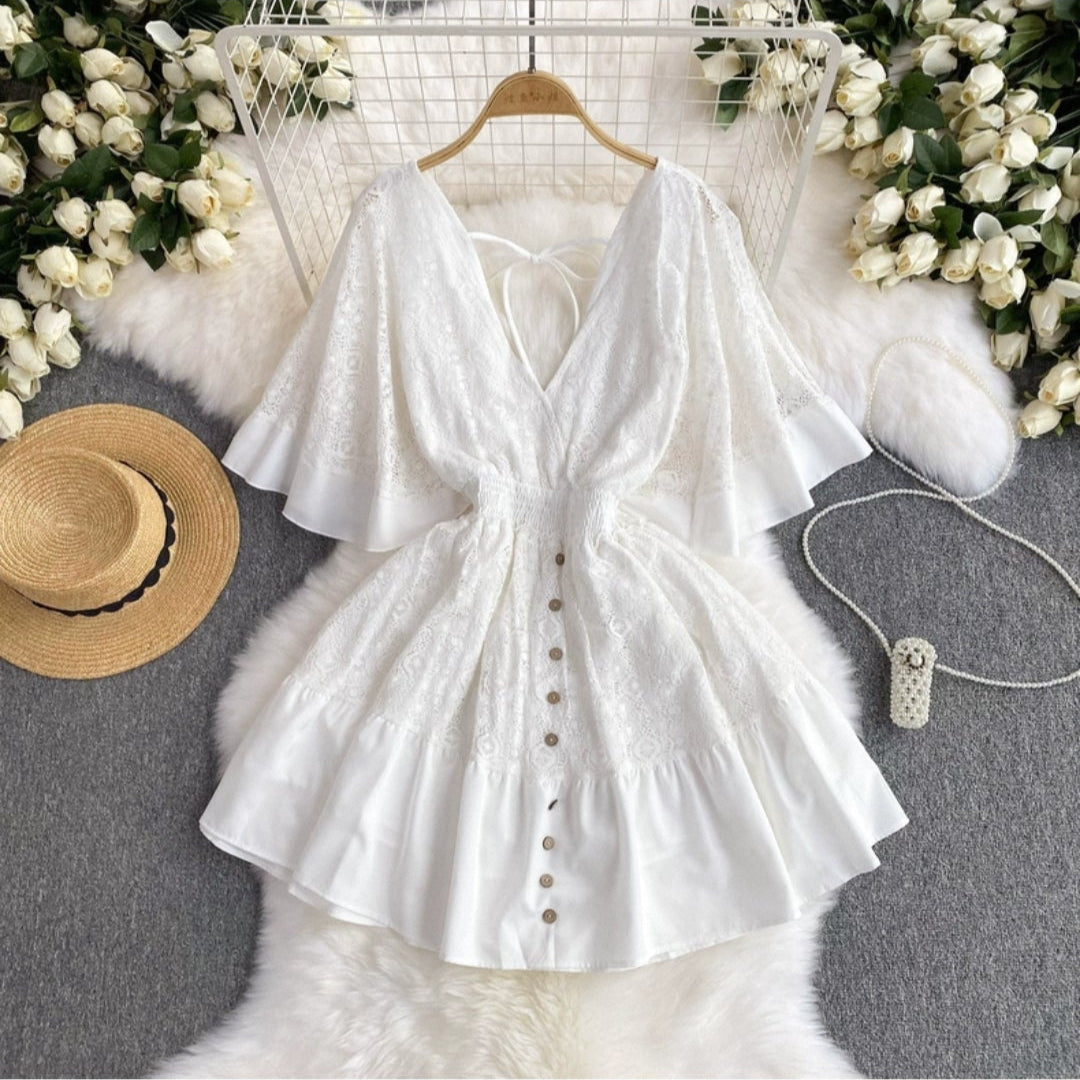 White boho chic summer dress with button front and flowy sleeves by Orchid Moda displayed with a straw hat and floral decor