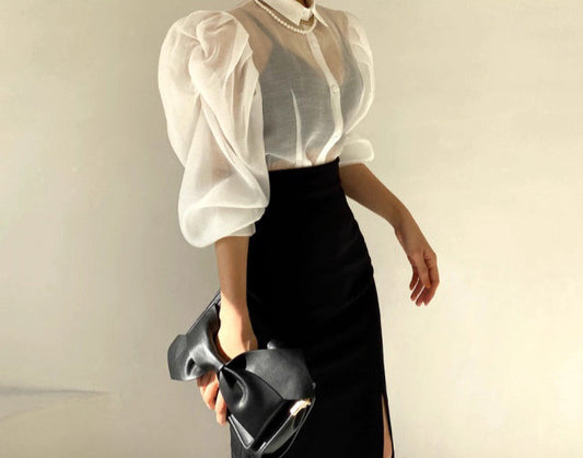 Orchid Moda chic sheer office blouse with puff sleeves paired with a black high-waist skirt and black clutch