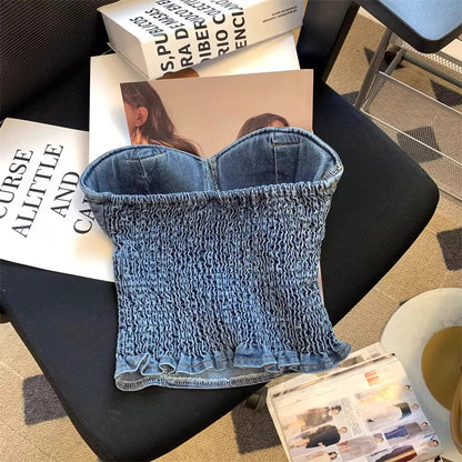 Denim tube top for women with smocked design and ruffled hem from Orchid Moda laid on black chair