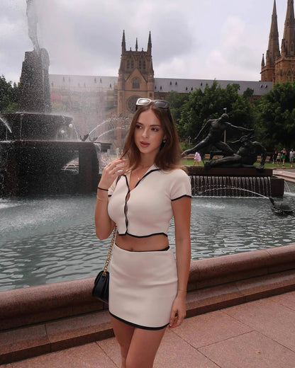 Woman wearing Orchid Moda beige desert co-ord set with black trim standing by a city fountain