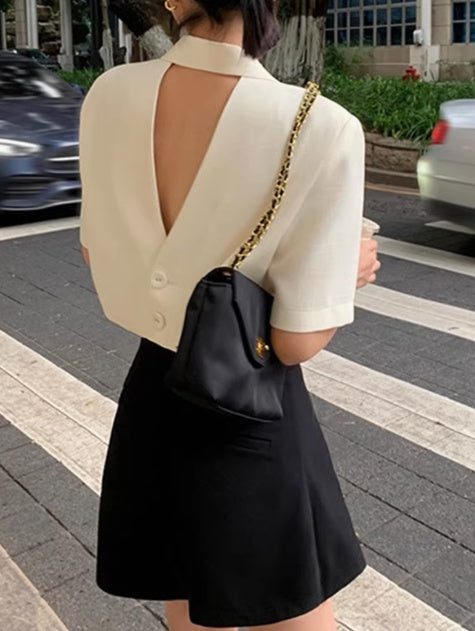 Woman wearing a formal open back top in cream paired with a black skirt and a black shoulder bag