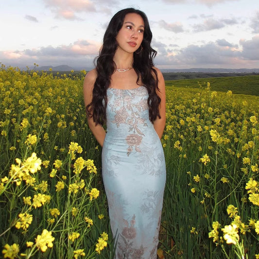 Orchid Moda frozen allure formal gown in light blue with floral patterns worn by model in yellow flower field