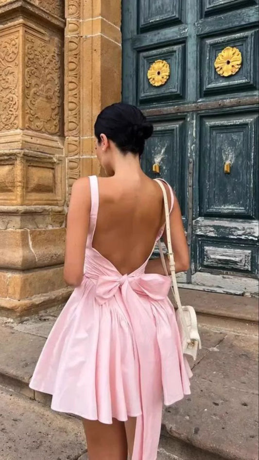 Woman wearing a pink knotted bow mini dress for women with an open back standing outdoors