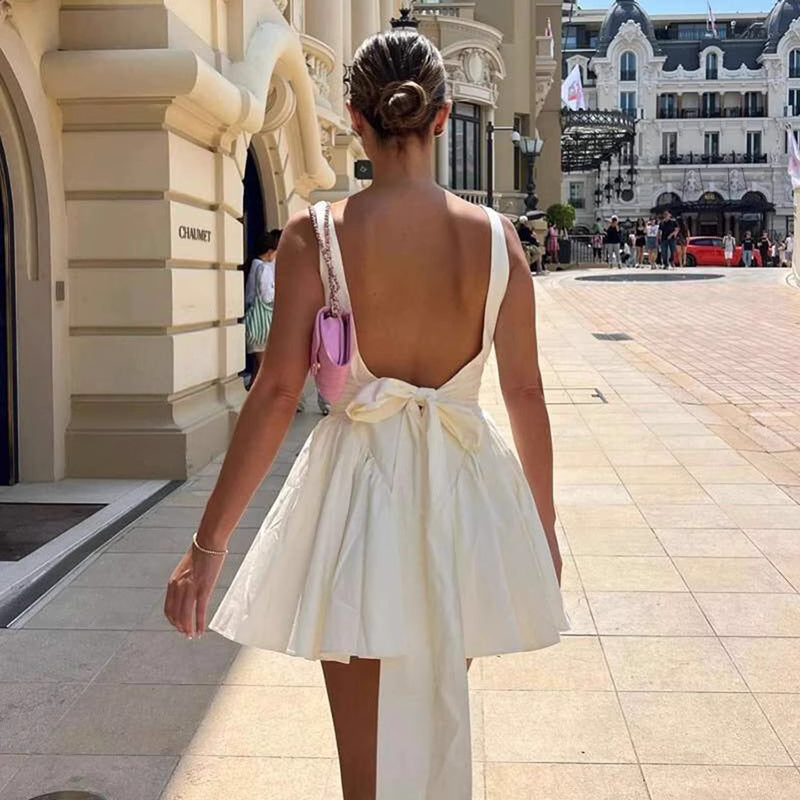 Back view of a woman wearing a white knotted bow mini dress for women by Orchid Moda on a city street