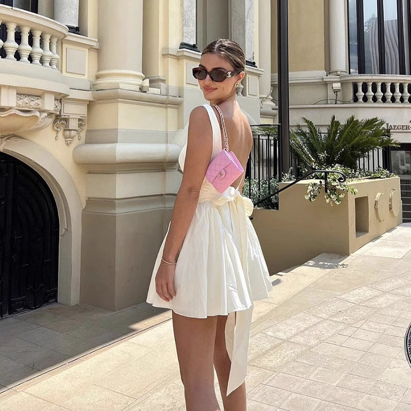 Woman wearing a white knotted bow mini dress for women by Orchid Moda with sunglasses and pink handbag outdoors