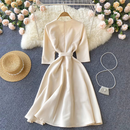Orchid Moda almondine midi dress in beige with belt detail displayed with straw hat and pearl purse