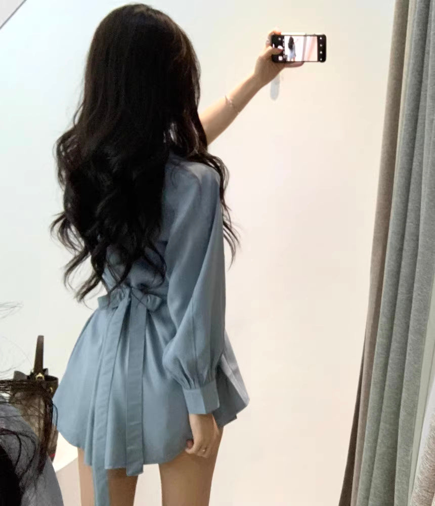 Woman wearing a blue retro co-ord set with long sleeves and waist tie taking a mirror selfie