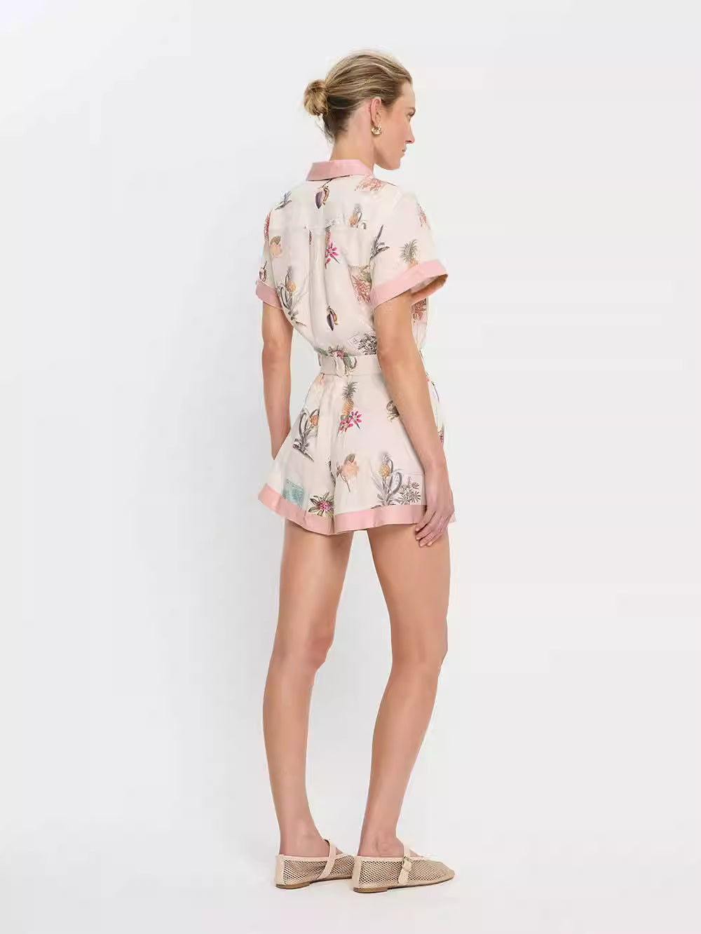 Orchid Moda short sleeve linen romper with floral print and pink trim worn by model from back