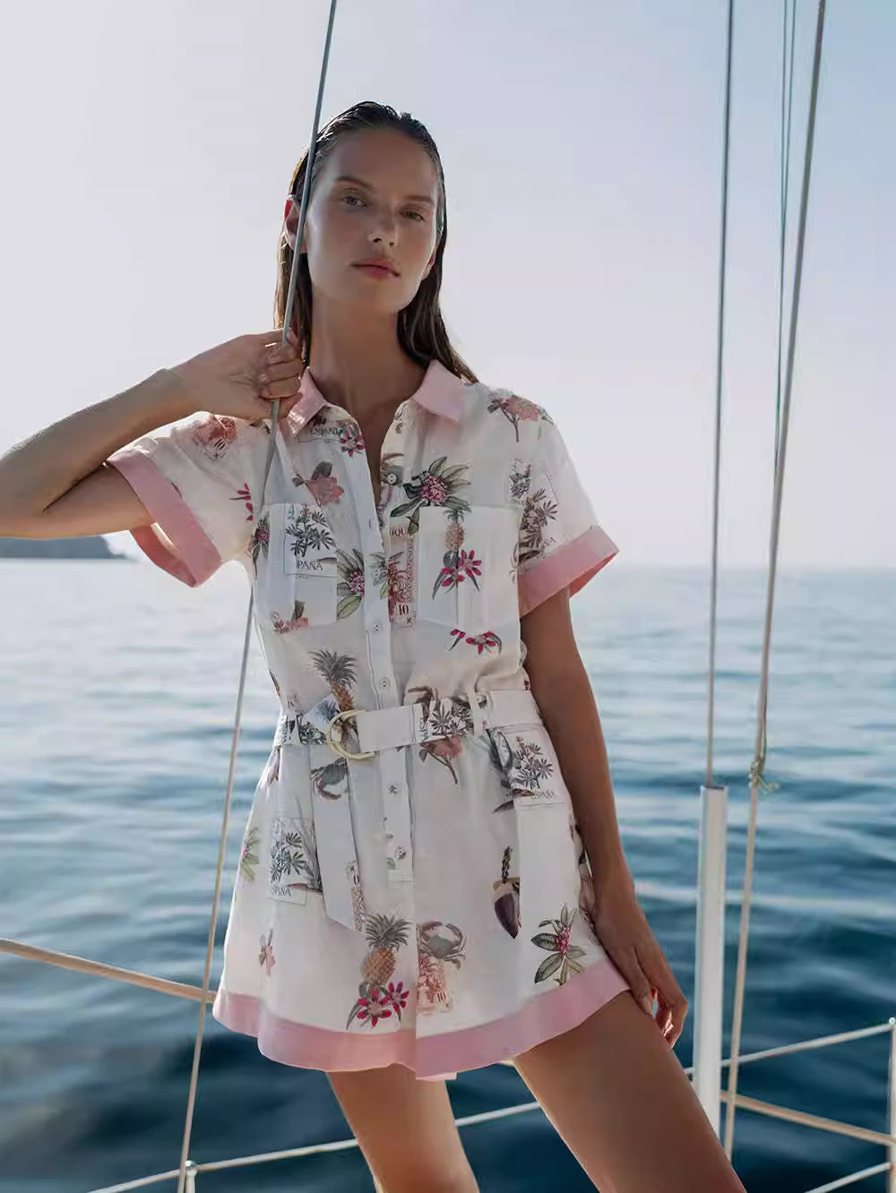 Orchid Moda short sleeve linen romper with tropical print and belted waist worn by woman on a boat