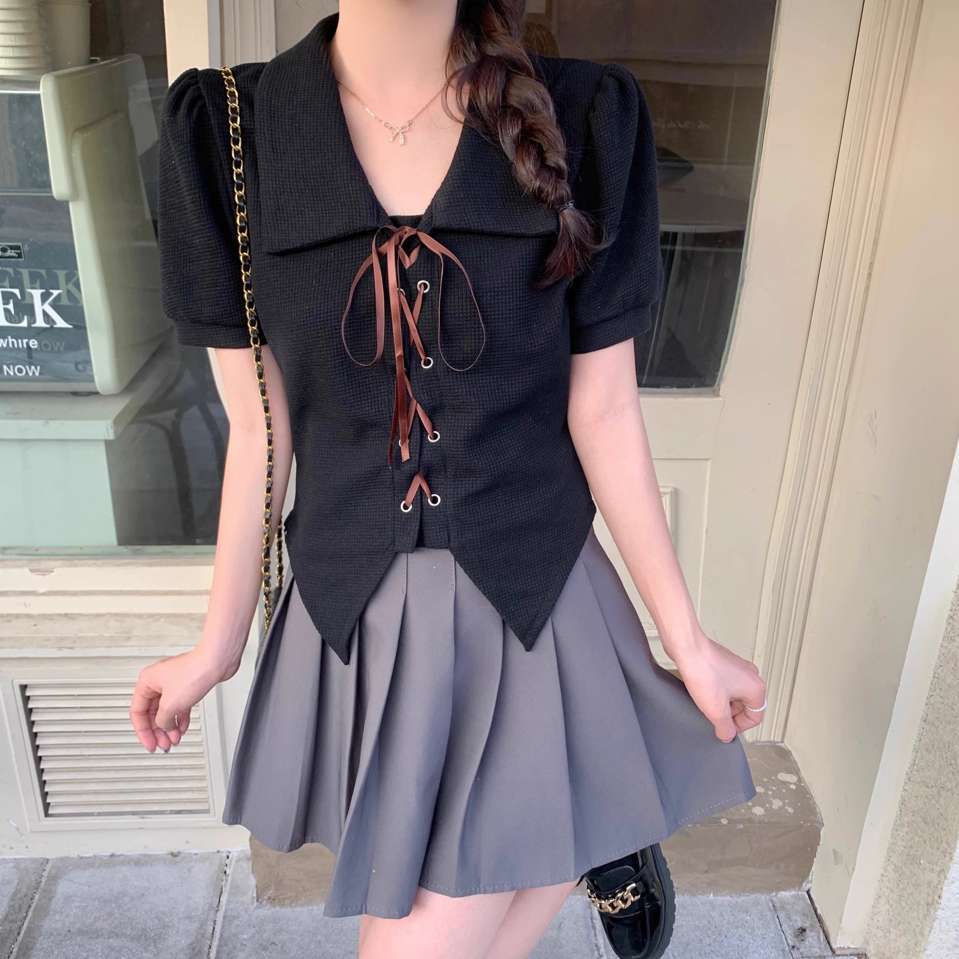 Orchid Moda black short sleeve statement shirt with lace-up front and puff sleeves worn with gray pleated skirt