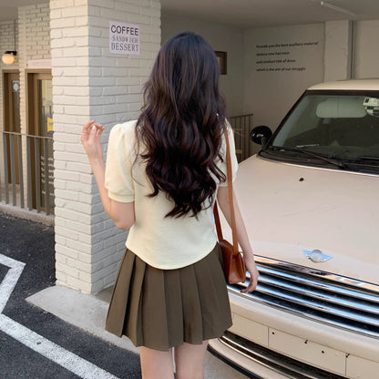 Orchid Moda short sleeve statement shirt in cream worn with a pleated skirt outdoors near a vintage car