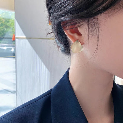 Trendy geometric earrings for women in matte gold worn by a woman with dark hair and navy blazer