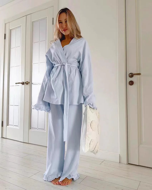 Woman wearing light blue comfortable lounge wear pajamas with belt and ruffled sleeves standing indoors