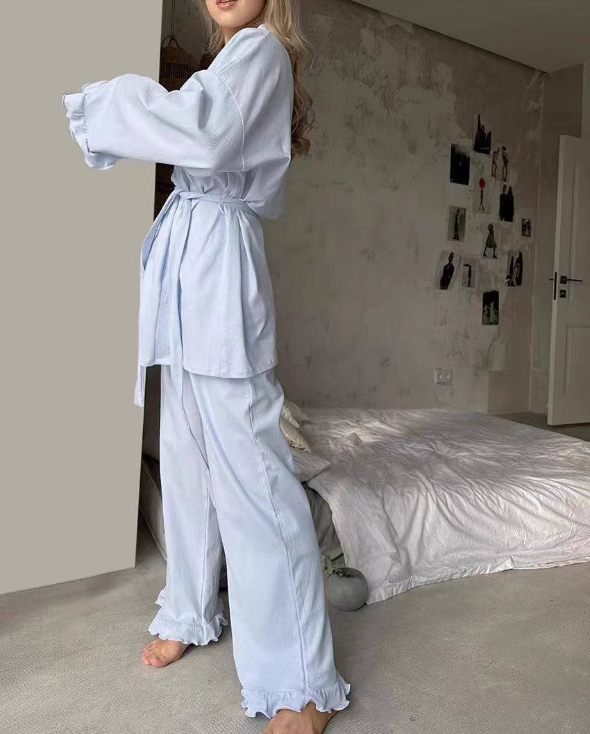 Woman wearing comfortable lounge wear pajamas in light blue standing next to a bed in a cozy room