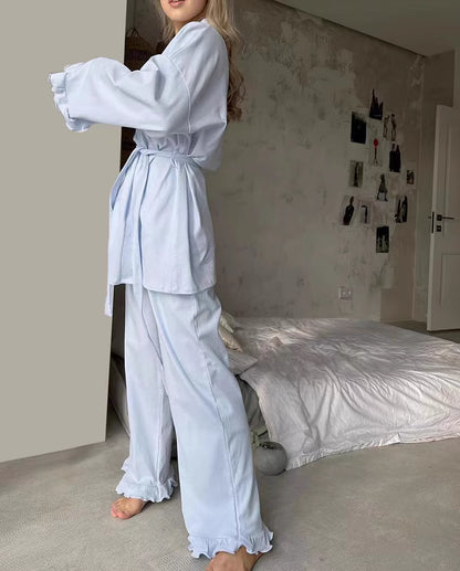 Woman wearing comfortable lounge wear pajamas in light blue standing next to a bed in a cozy room
