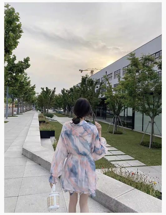 Woman wearing a flowy summer co ord set with pastel colors walking outdoors holding a white handbag