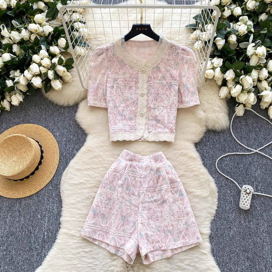 Orchid Moda vintage rosette shorts set with floral print and button-up top laid flat with straw hat and flowers
