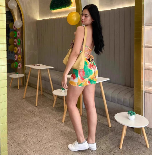 Woman wearing a colorful watermelon print bodycon dress with open back and white sneakers indoors
