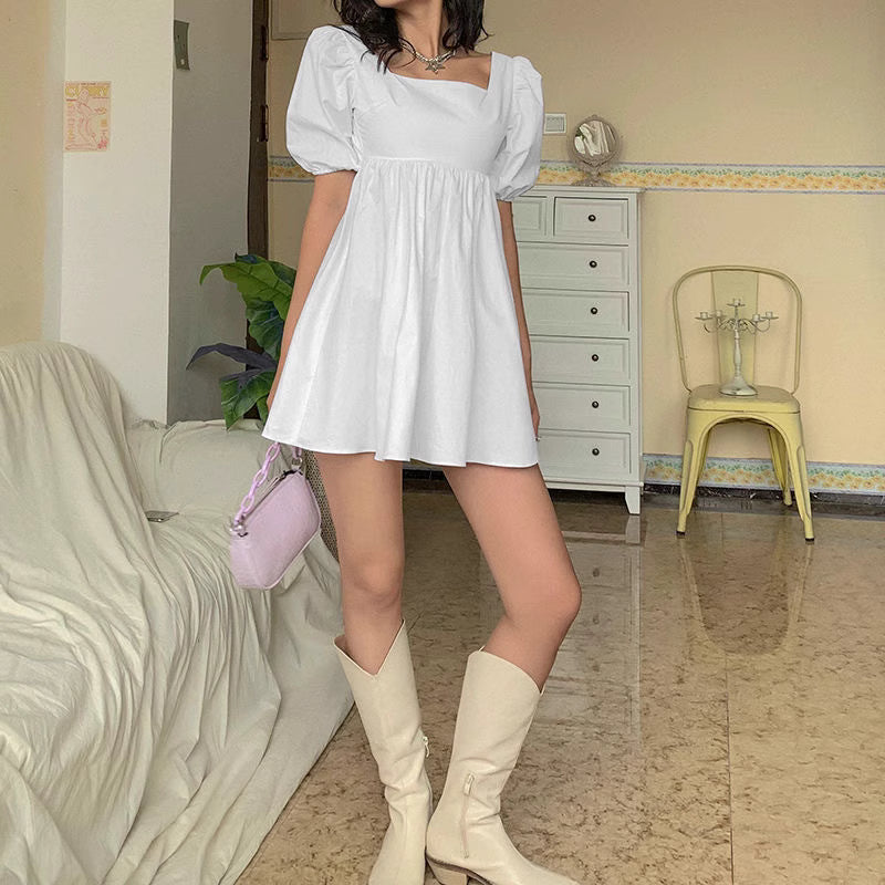 Orchid Moda white backless dress with puff sleeves styled with white boots and a lavender handbag