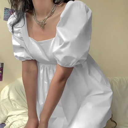 Orchid Moda white backless dress with puff sleeves and square neckline on a seated model