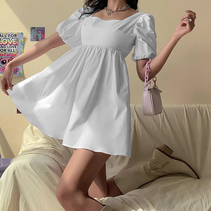 Orchid Moda white backless dress with puff sleeves and fitted bodice styled with boots and a handbag